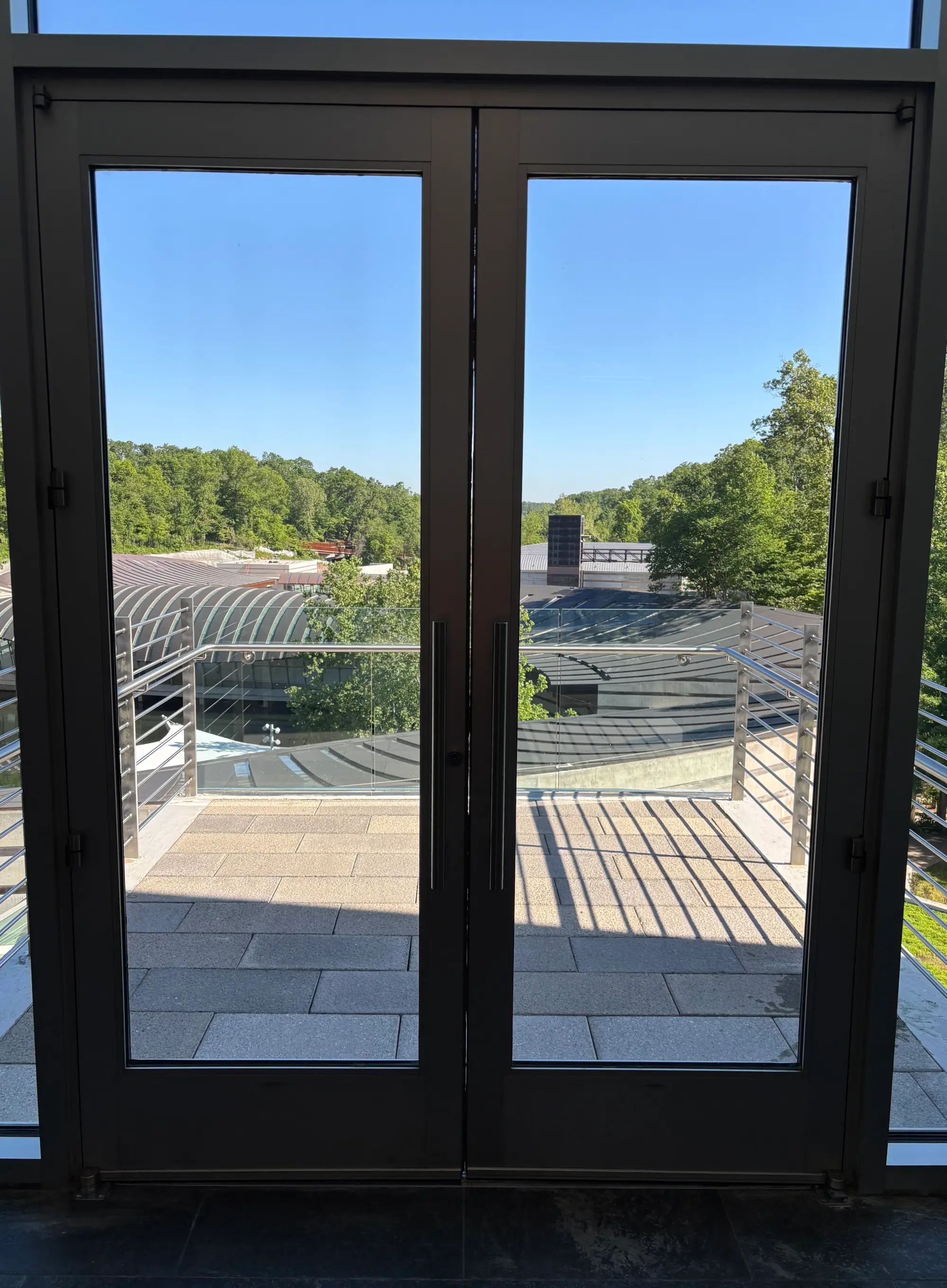 Commercial glass double doors with black metal frames opening to an outdoor balcony.