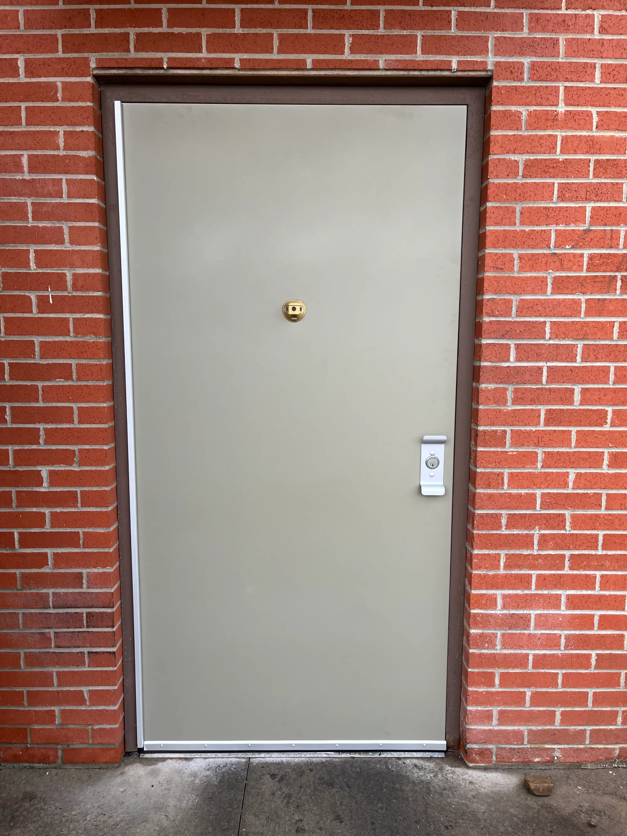Commercial metal service door with exterior lock hardware installed in a brick building.