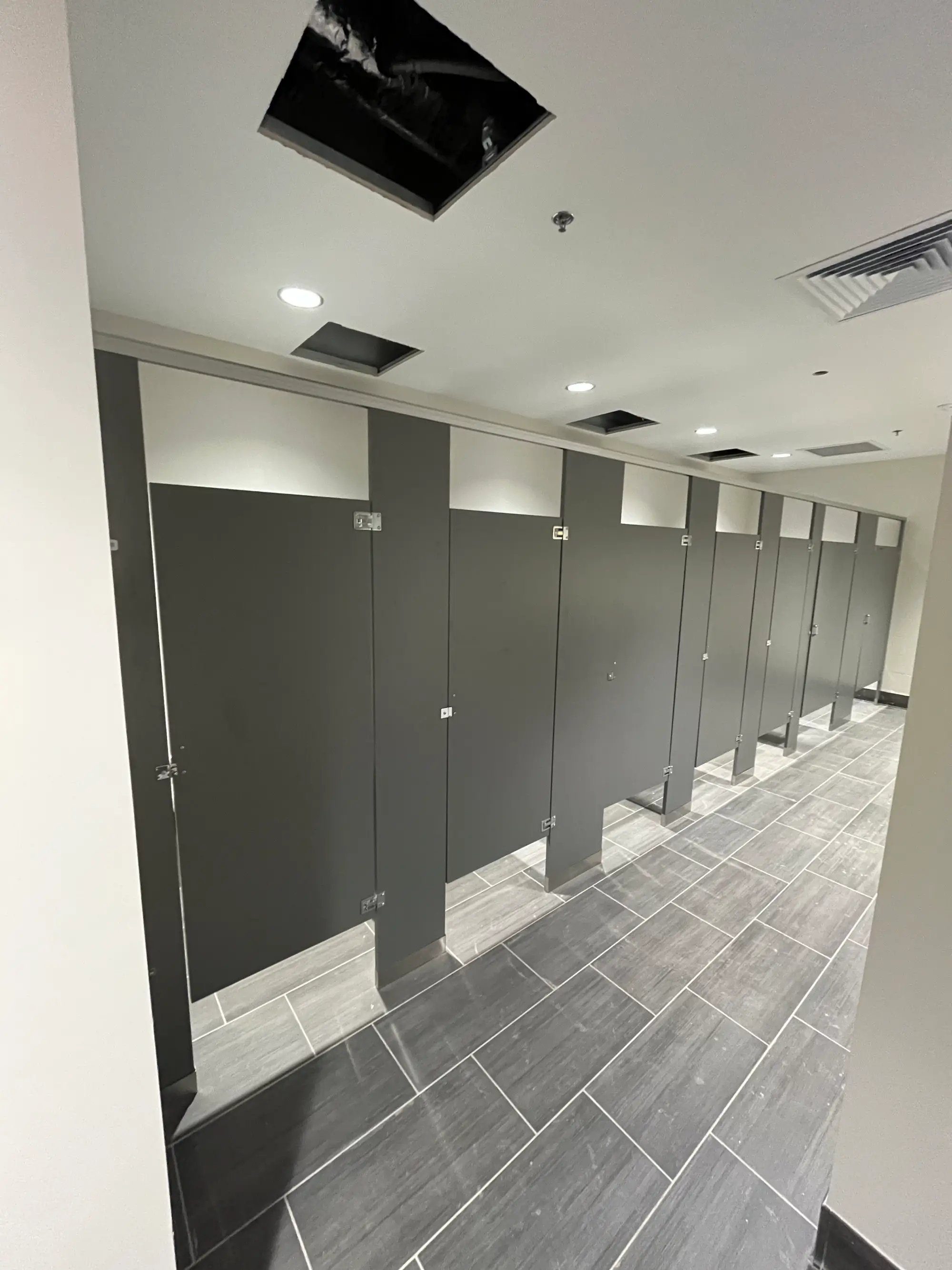 Commercial restroom partition installation with gray stall doors and hardware in a modern bathroom.